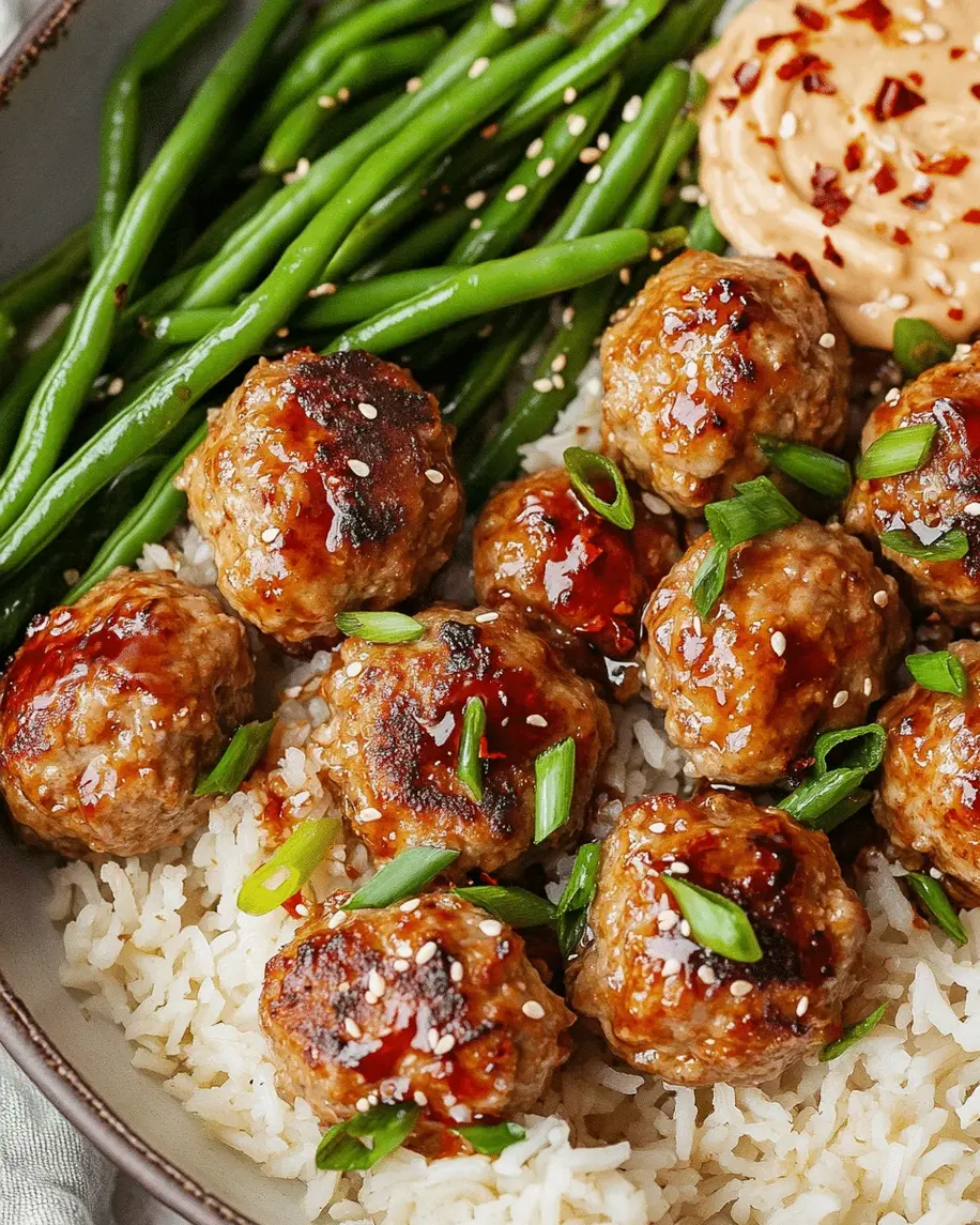 Plated firecracker meatballs atop coconut rice with green beans, garnished and ready to serve.