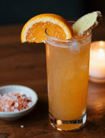 Cortisol balancing mocktail recipe in amber glass on dark walnut wood with orange slice and ginger