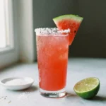 Watermelon electrolyte drink recipe sea salt in a tall glass with sea salt rim and fresh watermelon wedge on marble counter