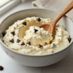 Bowl of cottage cheese cookie dough with chocolate chips, served with a spoon on a marble surface